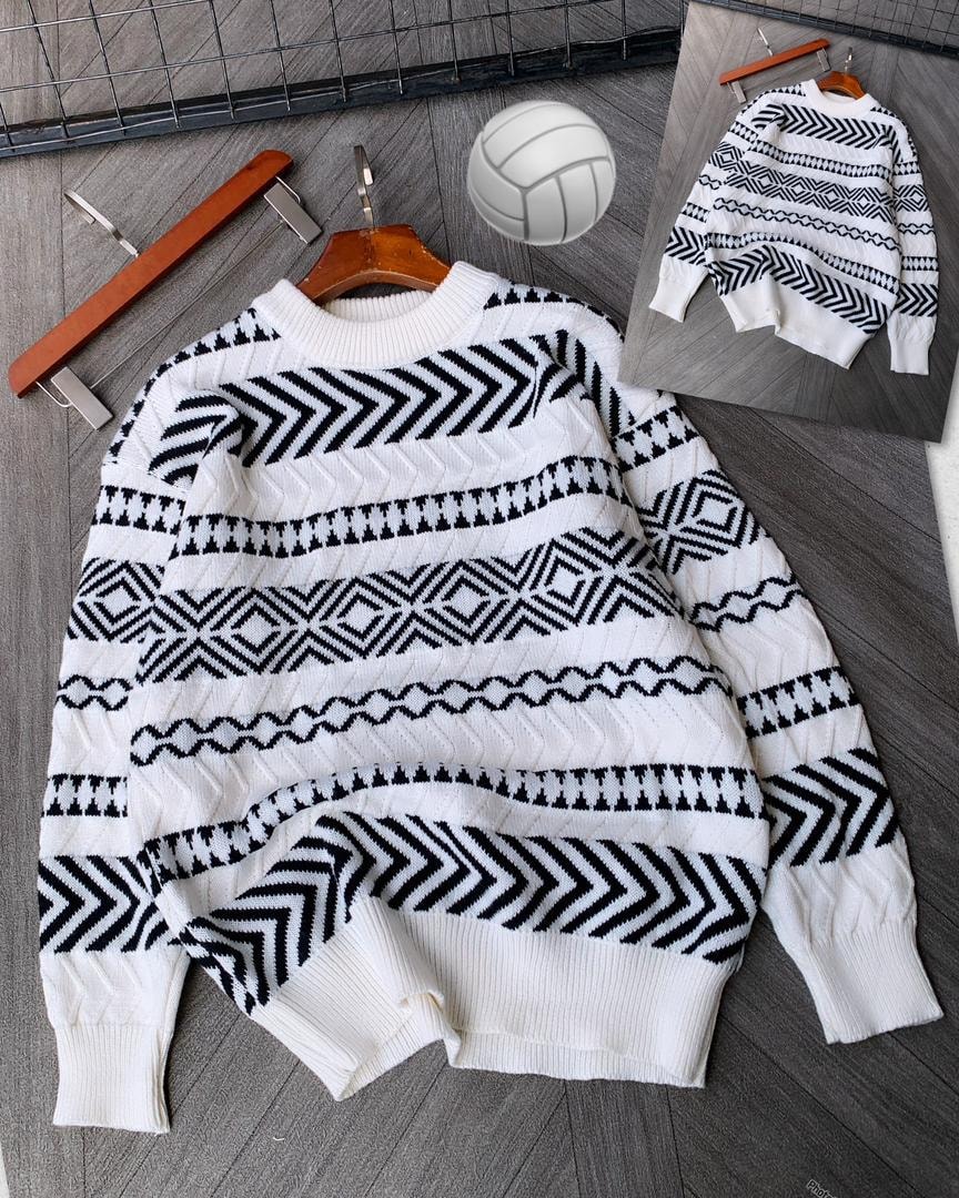 White geometric patterned knitted sweater on wooden hanger with volleyball prop.