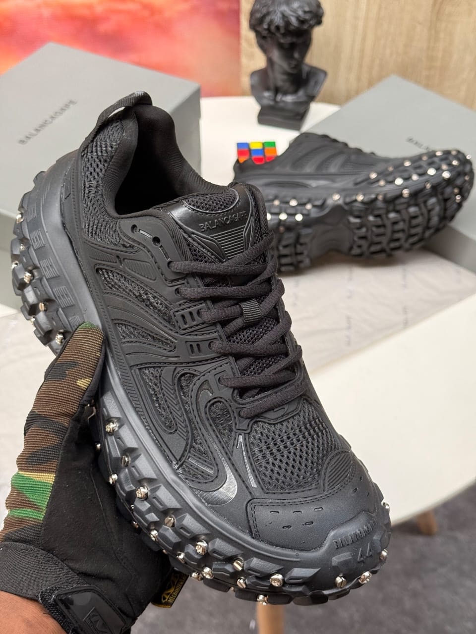 Black Balenciaga studded track sneakers held in hand showing detailed upper and sole.