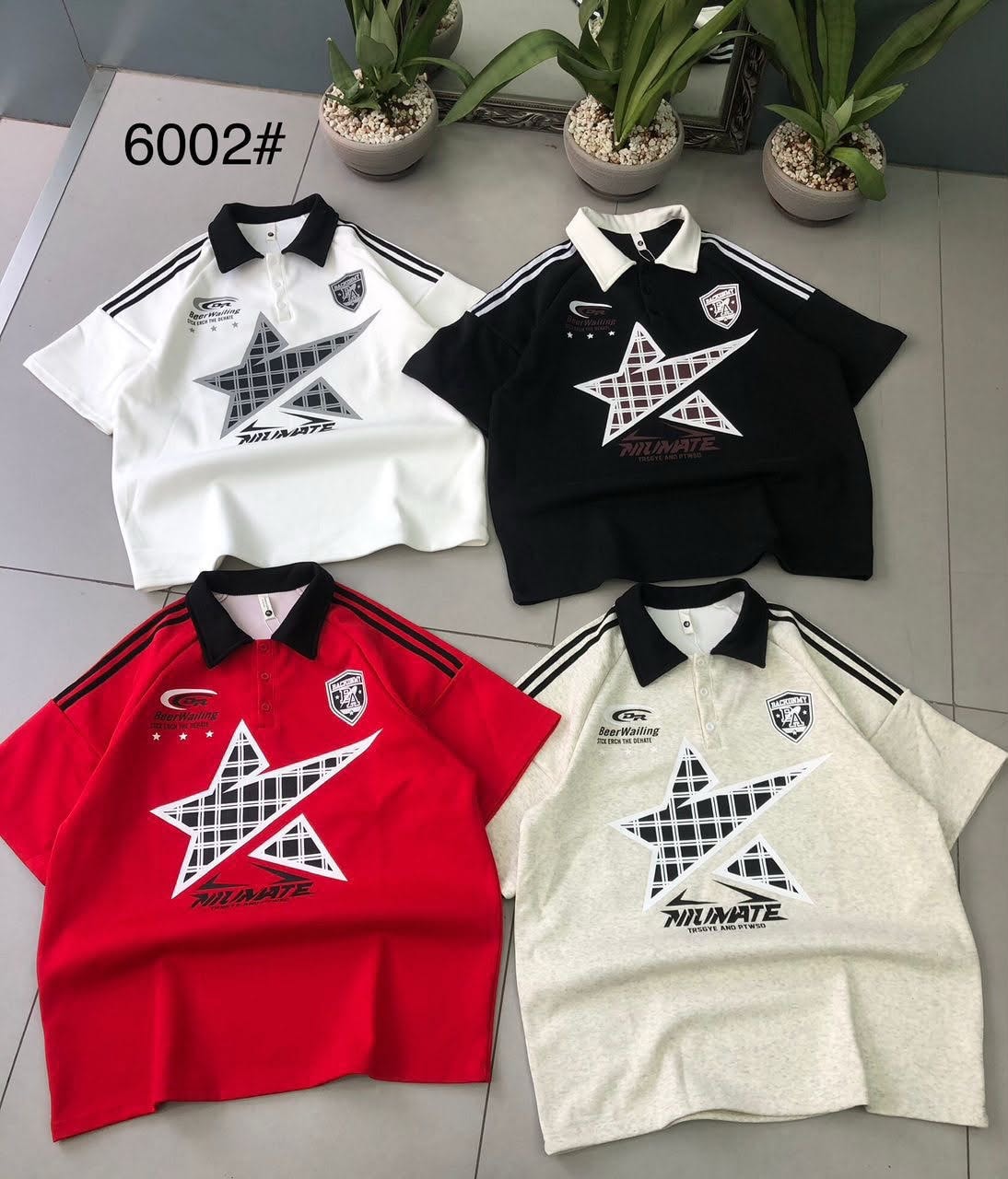 Four polo shirts in white, black, red and cream with large star prints, logos and striped sleeves laid flat.