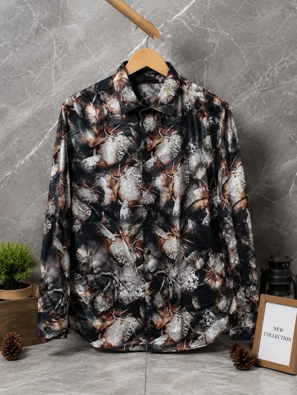 Long sleeve button-up shirt with black brown and white abstract leaf pattern hanging on wooden hanger against marble background.