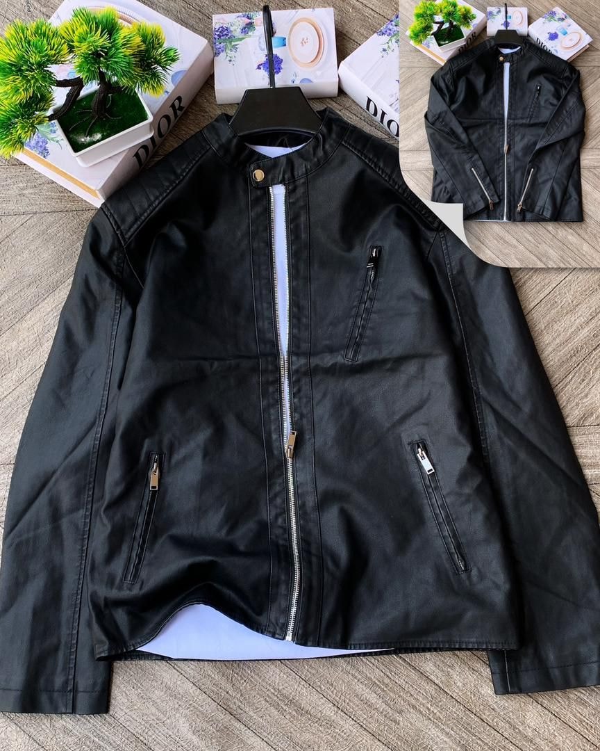 Black stand collar zip jacket laid flat on wooden surface with plants and decorative boxes.