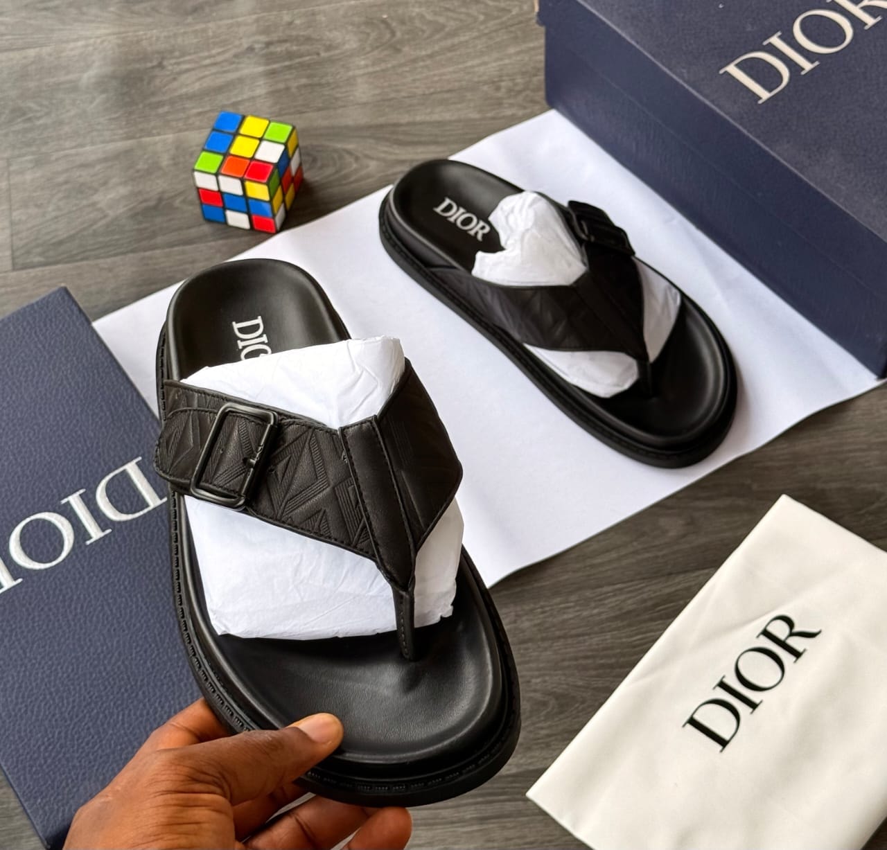 Black Dior slides with buckle and monogram embossing, shown with branded box and dust bag.