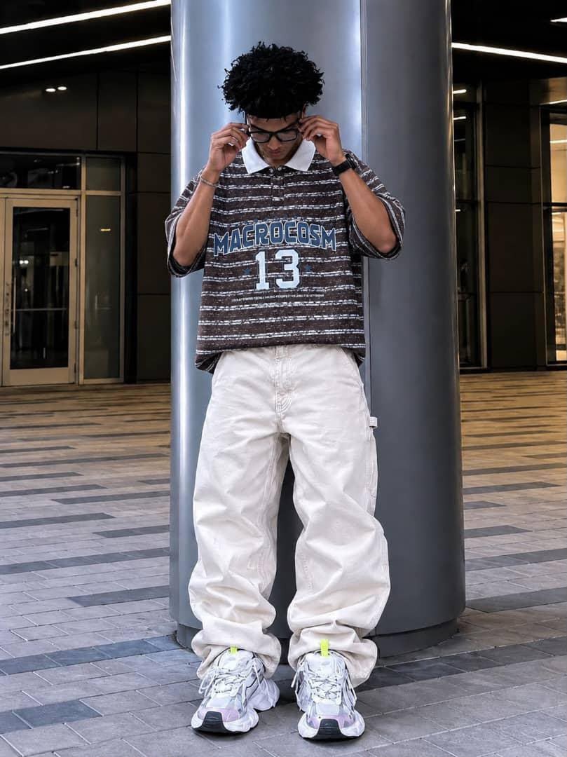 Model wearing brown striped MACROCOSM 13 polo shirt with white cargo pants.