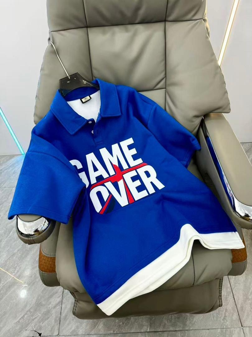 Blue GAME OVER polo shirt displayed on a chair.