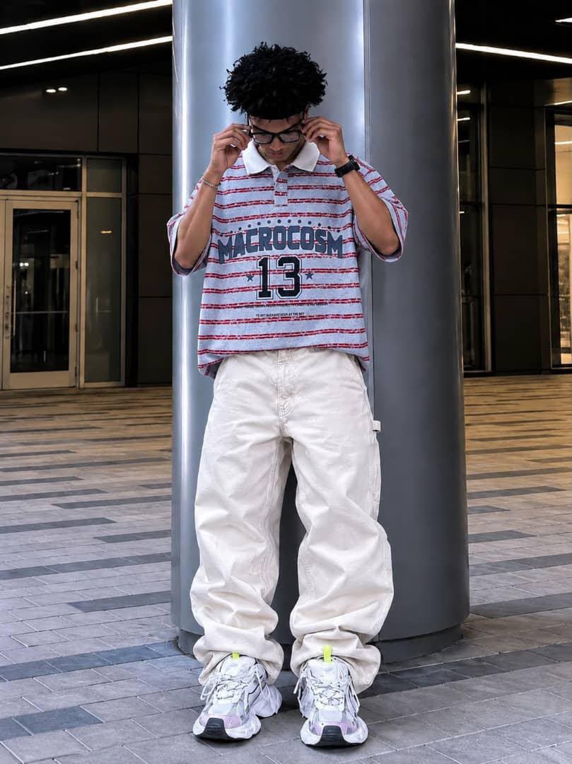 Model wearing light blue striped MACROCOSM 13 polo shirt with white cargo pants.