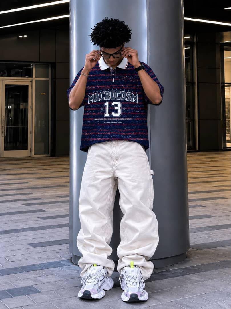 Model wearing blue striped MACROCOSM 13 polo shirt with white cargo pants.