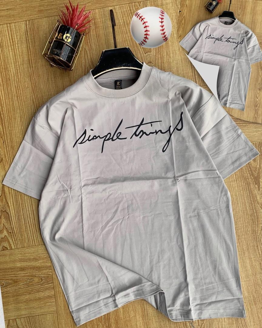 Light gray Simple Things cursive t-shirt on wooden floor with props.