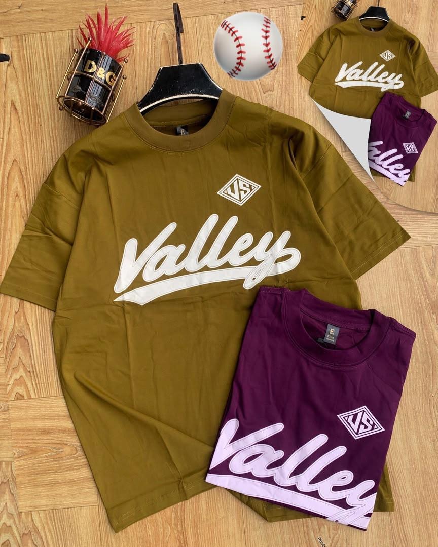 Olive and purple Valley script logo t-shirts with props on wood.