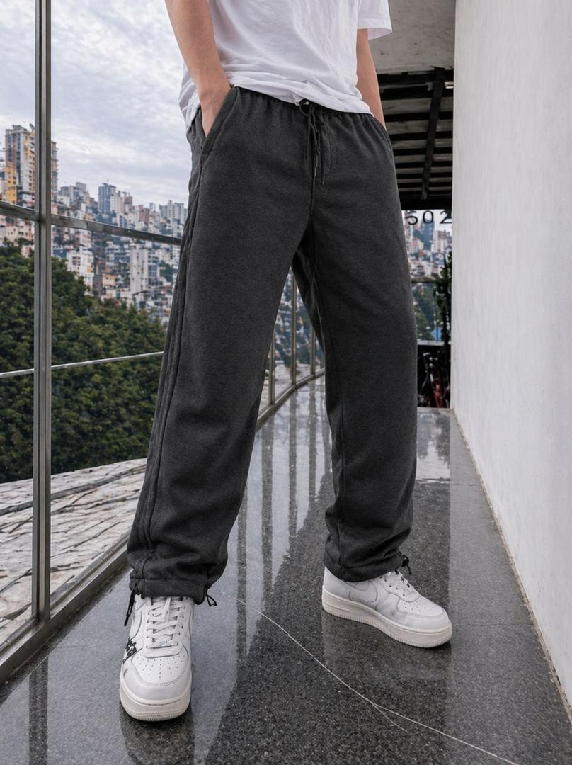 Model wearing dark gray fleece joggers with hands in pockets and white sneakers.