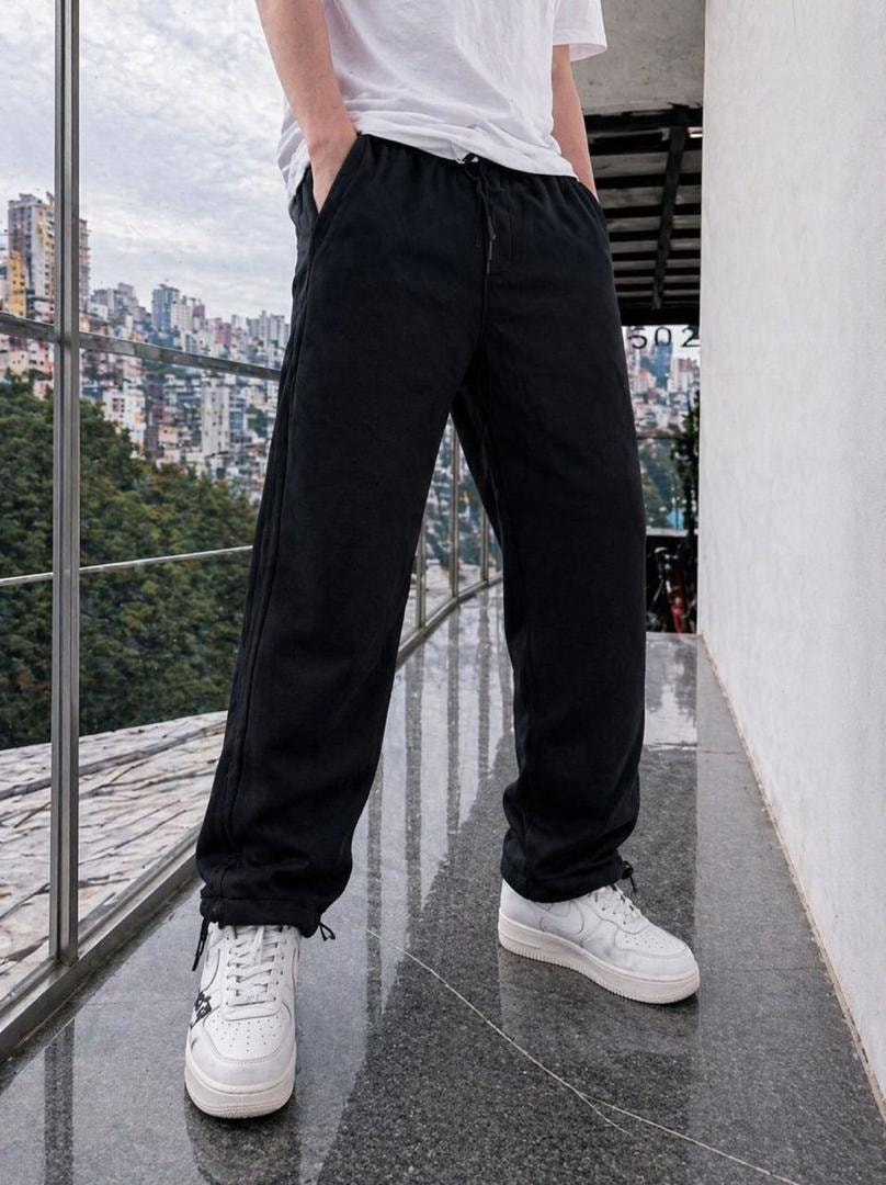 Model wearing black fleece joggers with hands in pockets and white sneakers.