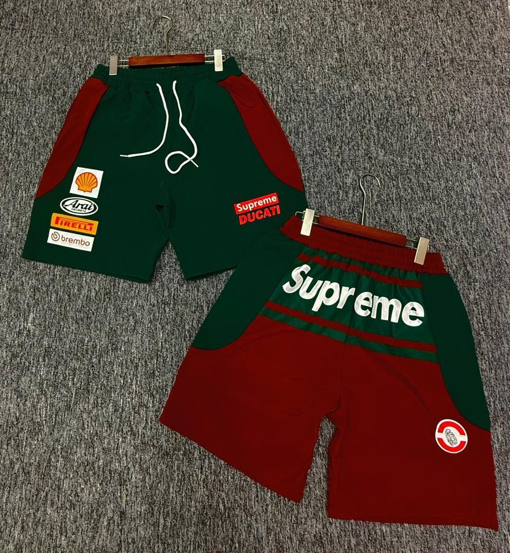 Two colorways of Supreme patch jogger shorts in green with red panels and red with green panels displayed on hangers.