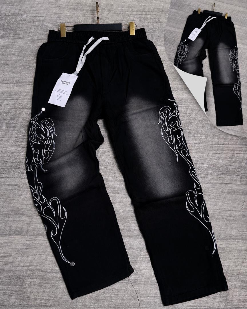 Black denim joggers with white side embroidery, faded panels and snap buttons.