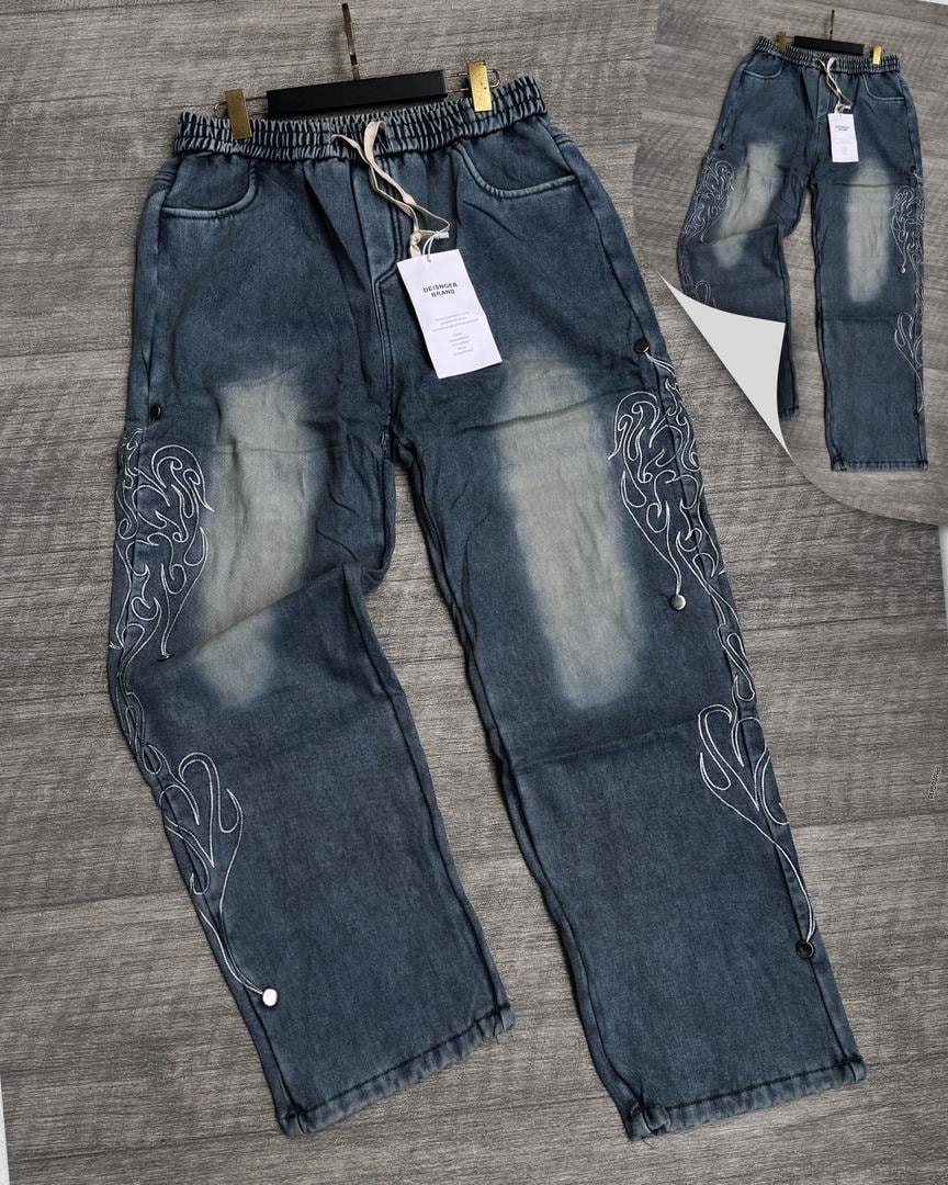 Blue denim joggers with white side embroidery, faded panels and snap buttons.