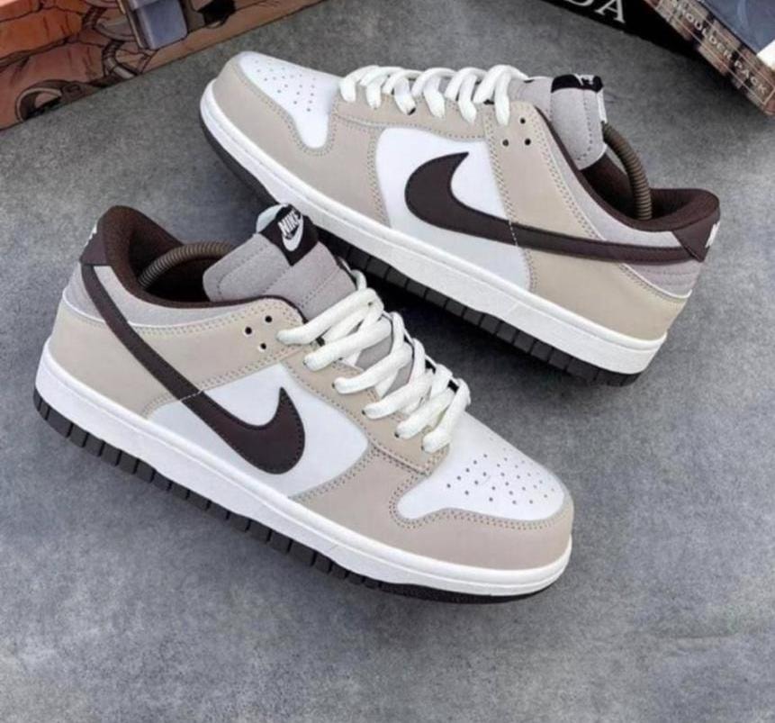 Beige, white, and brown Nike Dunk Low sneakers with dark Swoosh on gray background.