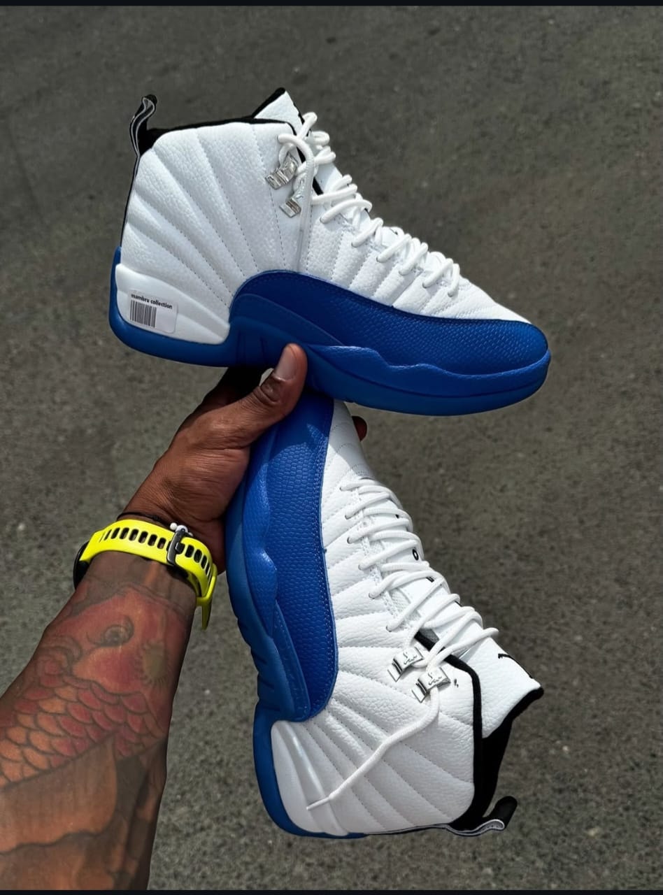 Air Jordan 12 high top sneakers in white blue and black held by hand outdoors.