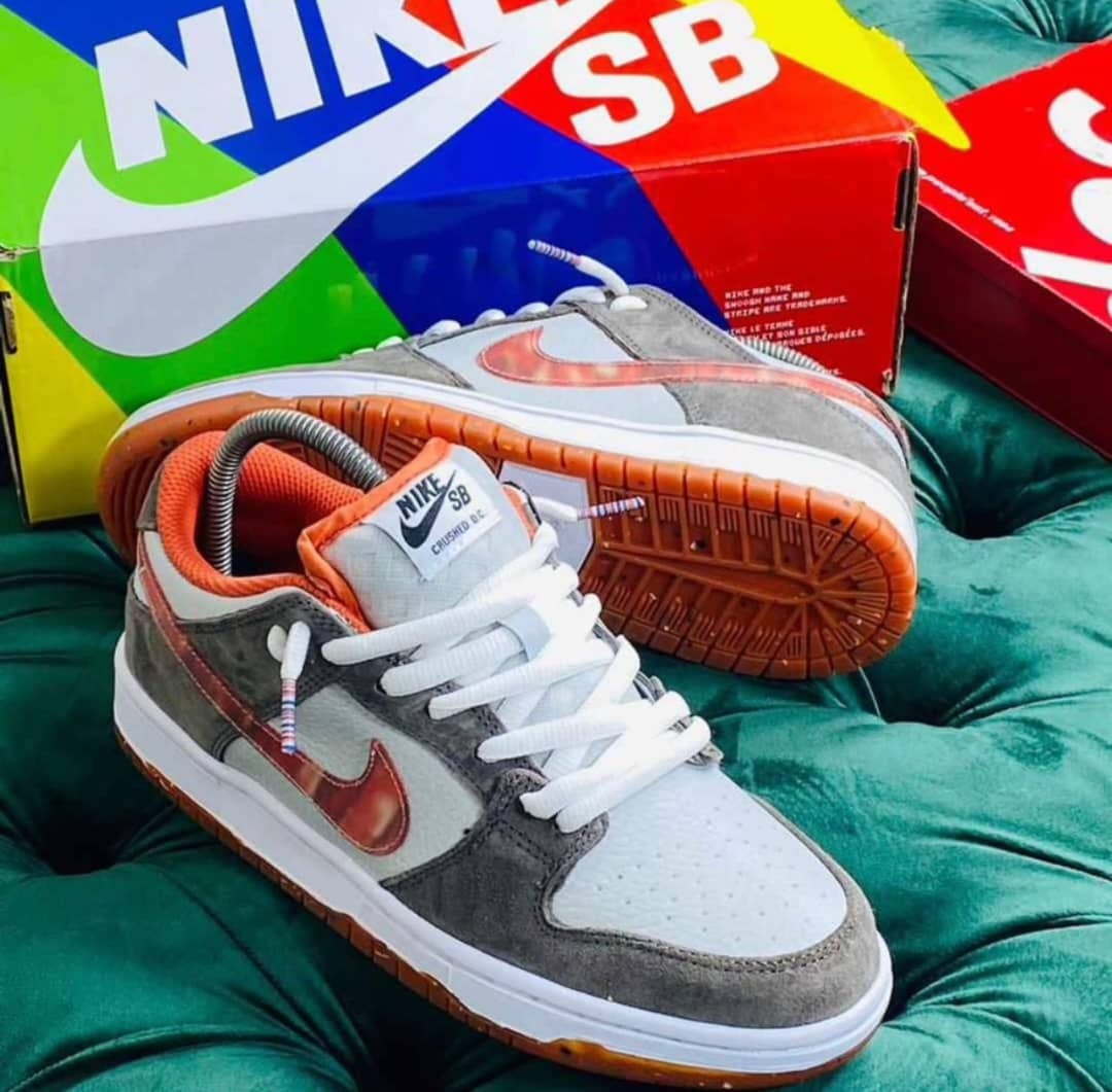 Nike SB Dunk Low in gray suede with orange swoosh on green surface with Nike SB boxes.