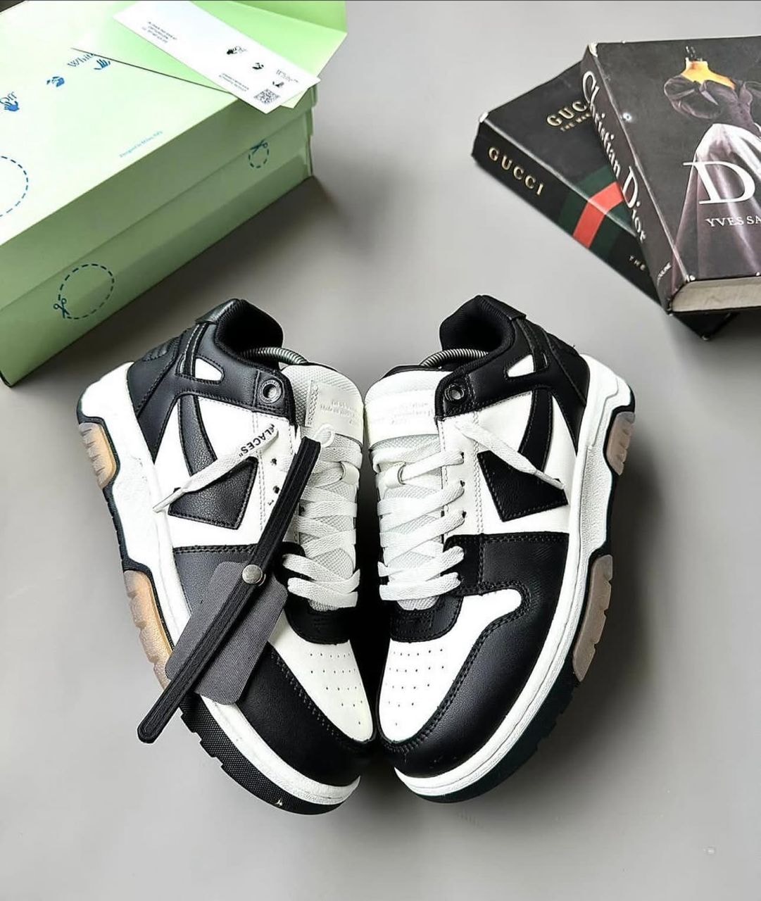 Black and white chunky sneakers with mixed materials and zip tie on gray background with green box and books.
