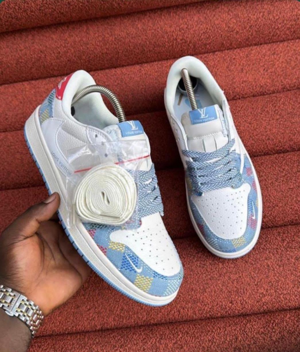 Hand holding white blue and multicolor monogram Nike low sneakers on red textured background.