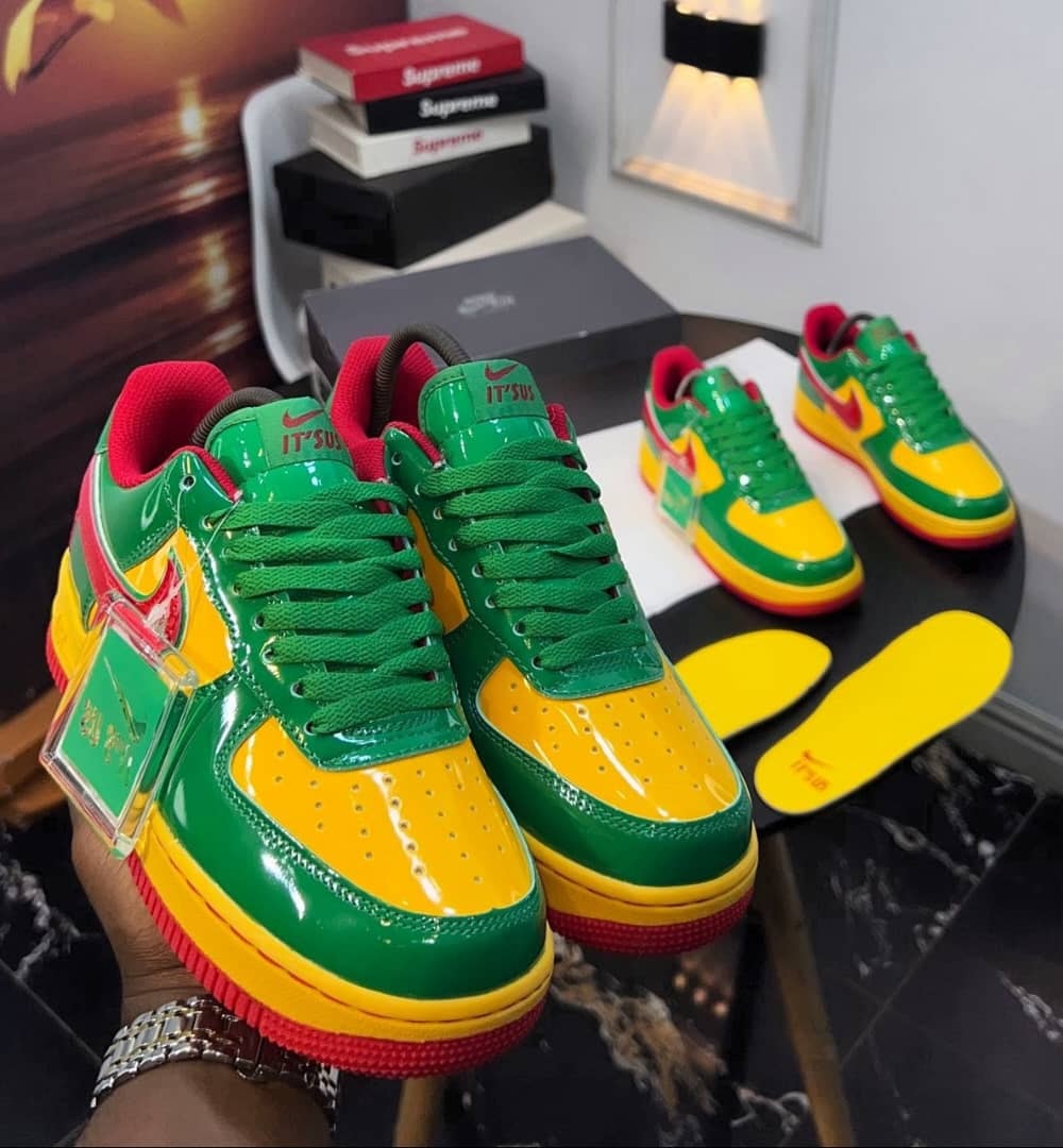 Hand holding green yellow and red Nike Air Force 1 sneakers with insoles and boxes in background.