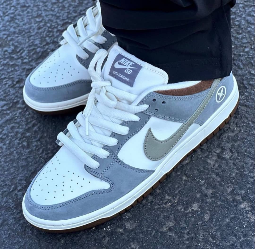 Person wearing white gray and brown Nike Dunk Low SB sneakers on paved ground.