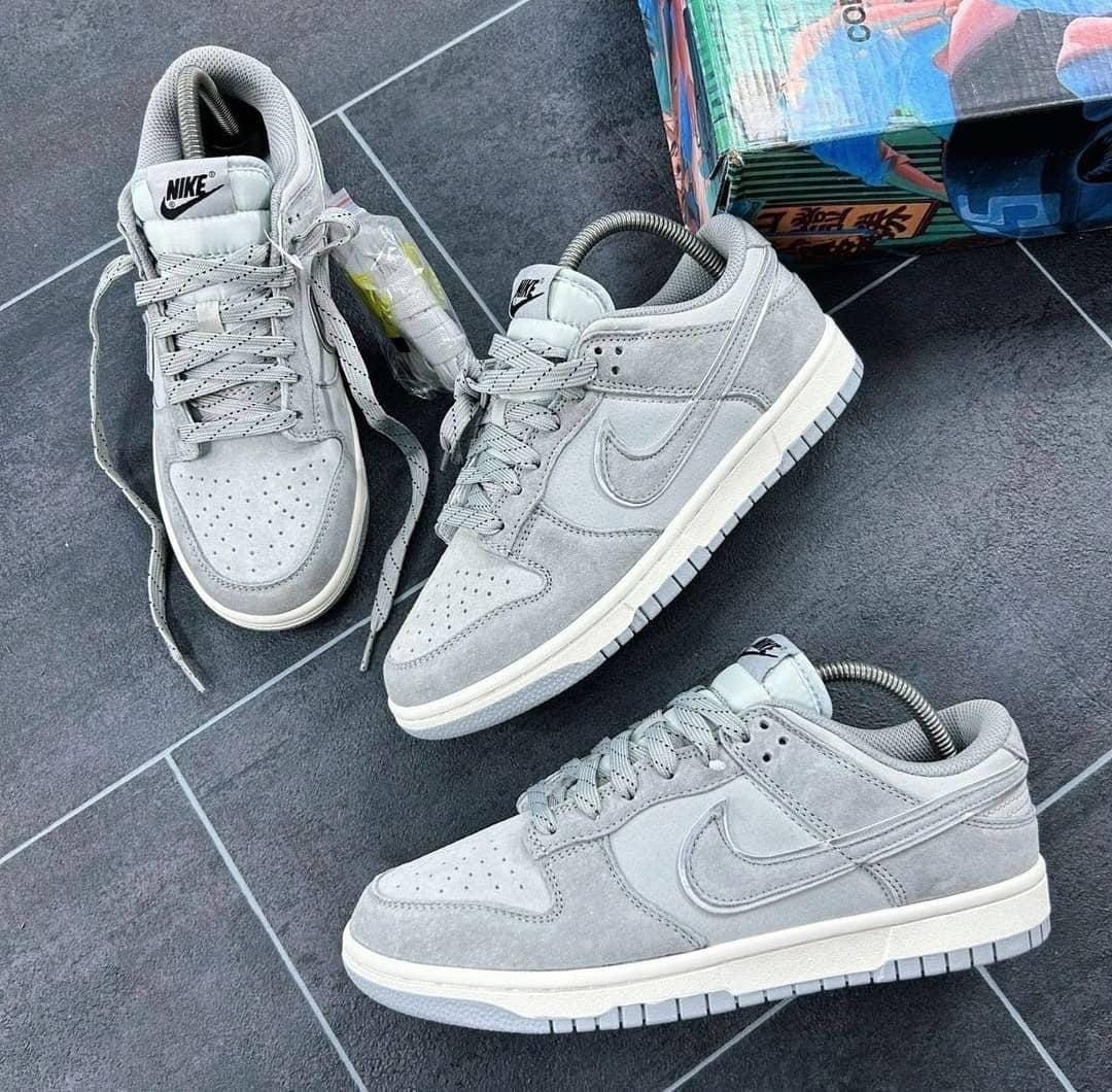 Gray Nike Dunk Low sneakers on tiled floor with colorful box.
