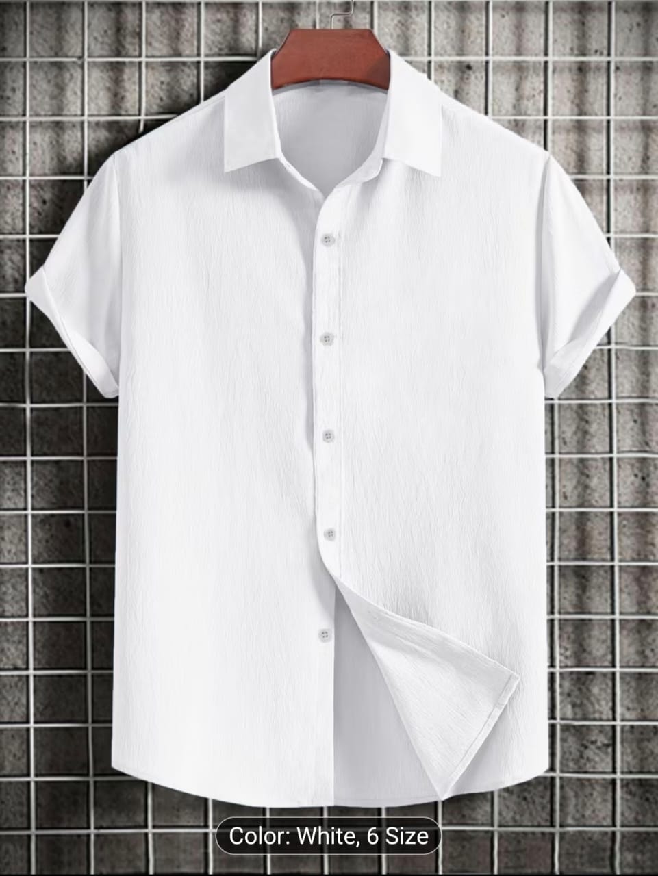 White short sleeve button-up shirt on wooden hanger against tiled wall.