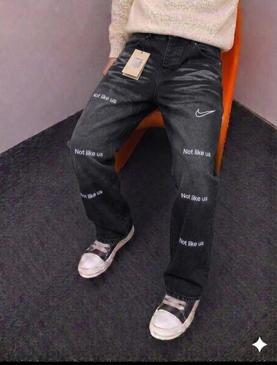 Model in black Not Like Us printed baggy jeans with swoosh, styled with cream knit top.