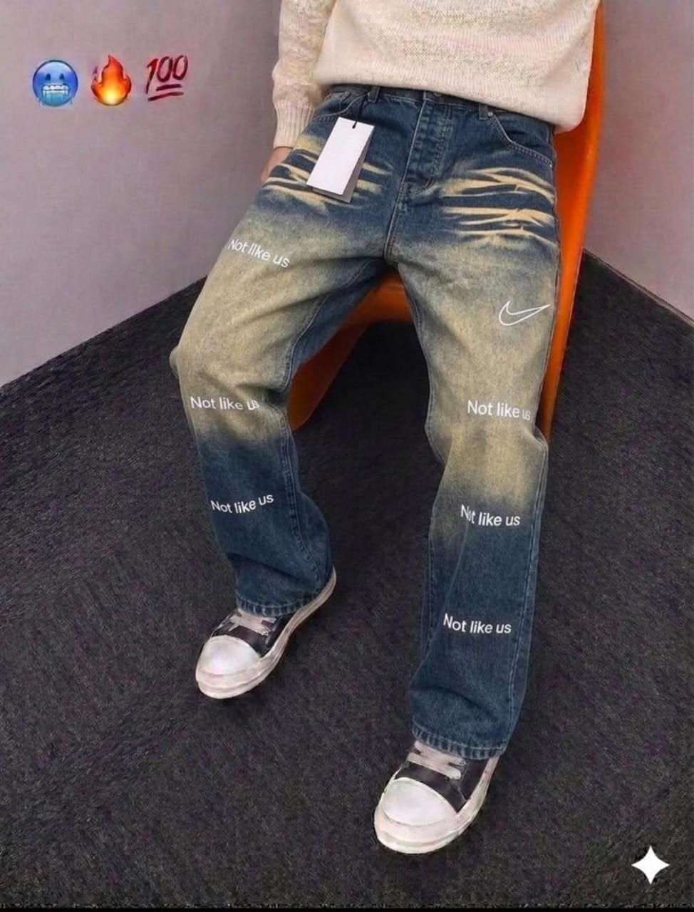 Model wearing blue faded Not Like Us graphic baggy jeans with cream sweater and sneakers.