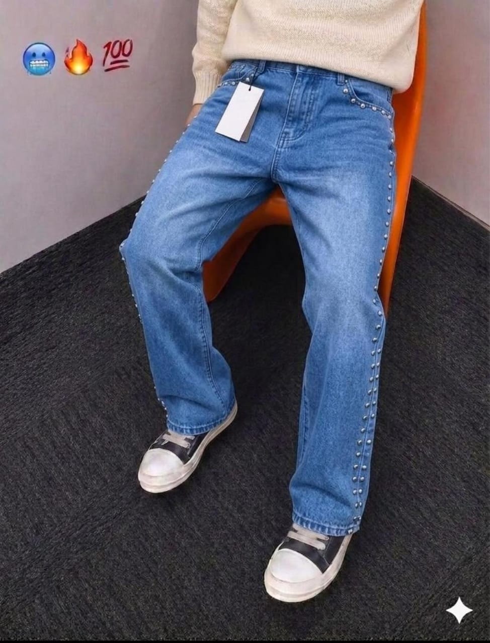 Model seated in blue baggy jeans with silver studs along side seams, paired with cream sweater.