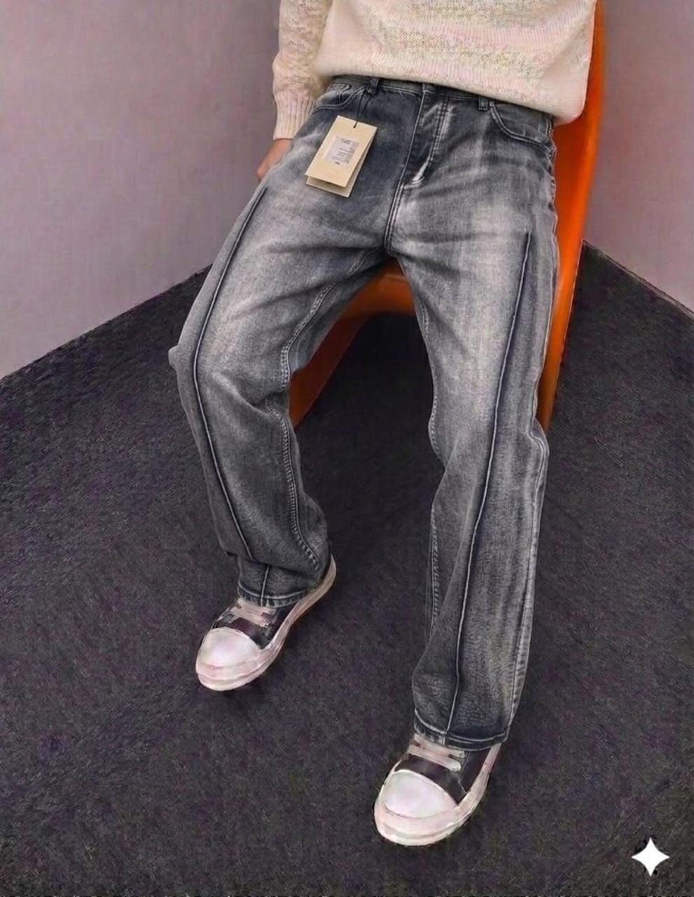 Person wearing faded gray baggy jeans with sweater and sneakers, seated on orange chair.