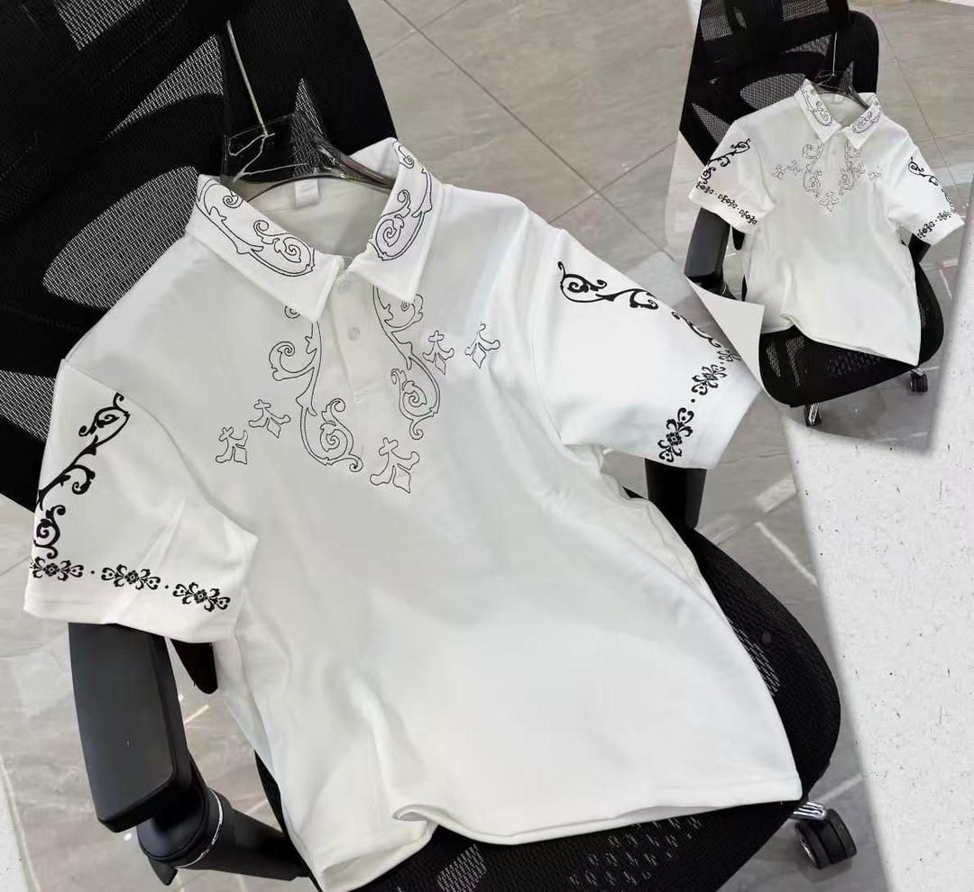 White polo shirt with black ornate embroidery on chest, sleeves and collar.