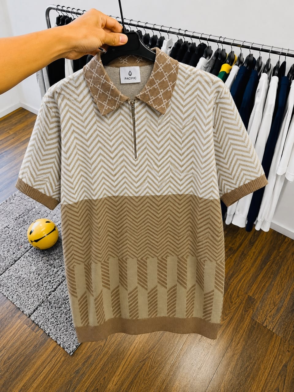 Beige and white chevron polo shirt on black hanger.