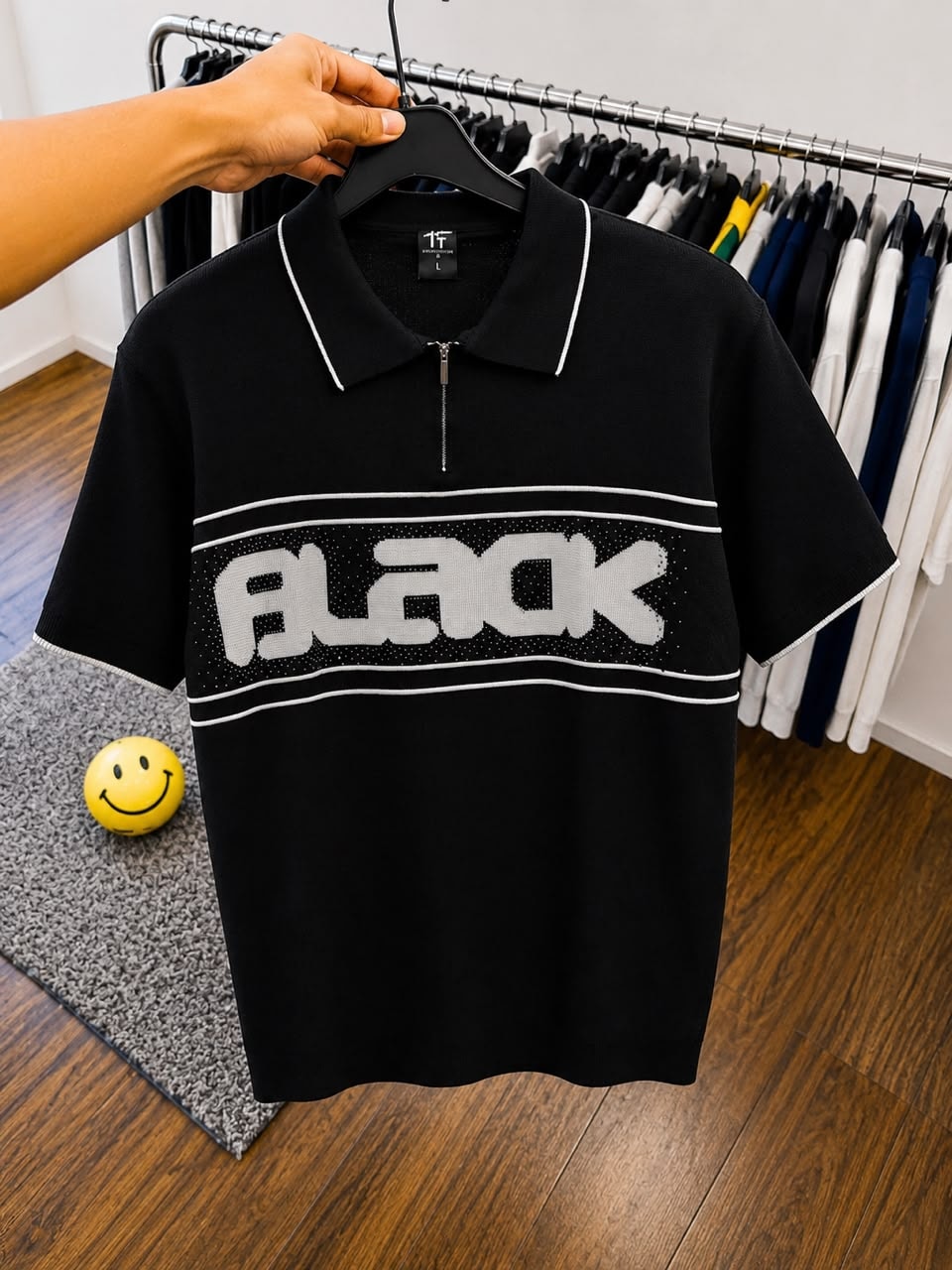 Black polo shirt with large white BLACK graphic on hanger.