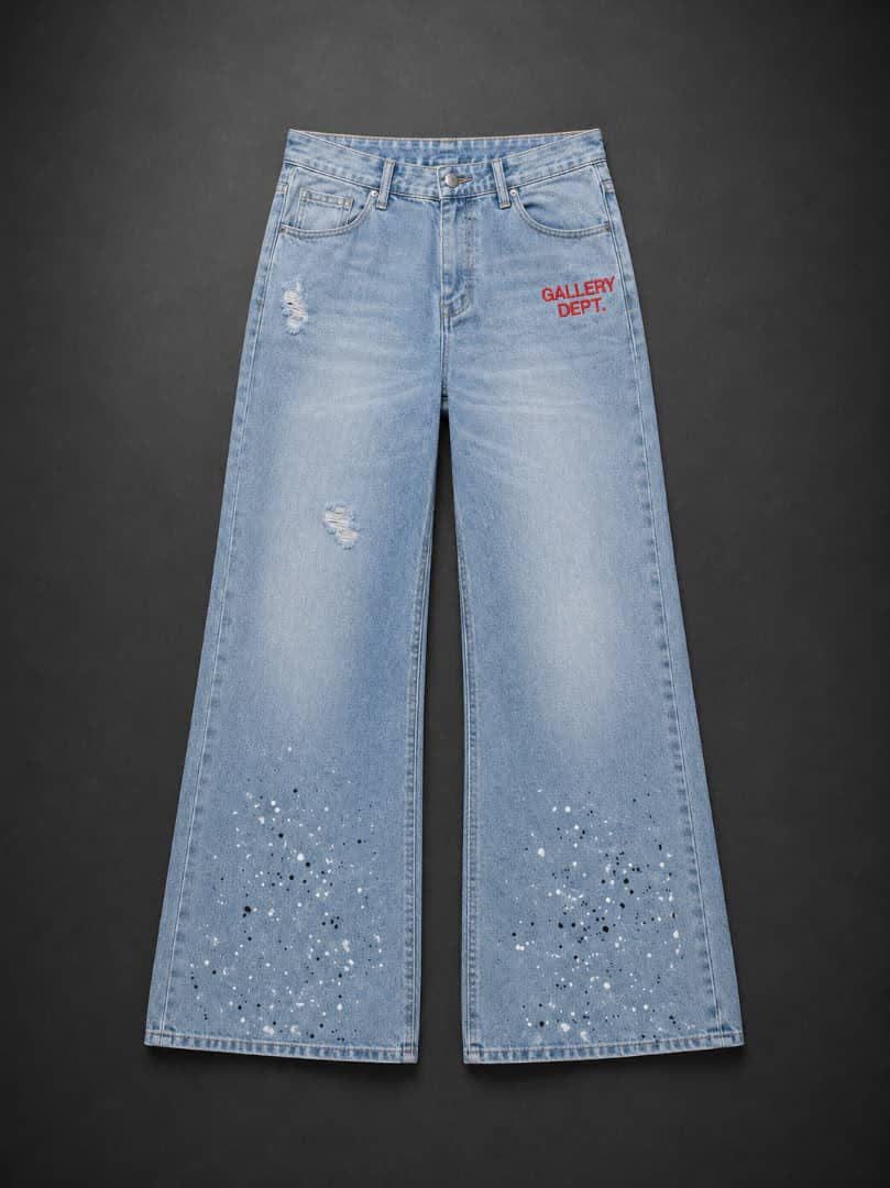 Light blue baggy jeans with Gallery Dept red text, small rips and paint splatter at the hem.