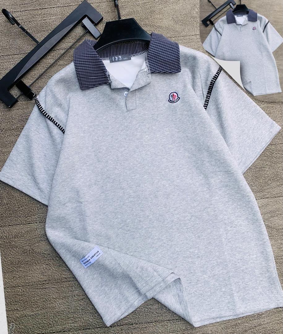 Light gray polo shirt with striped collar laid flat, showing chest logo and sleeve stitching.