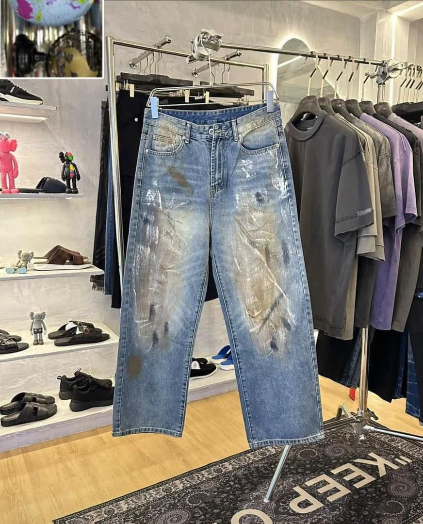 Blue baggy jeans with abstract white and brown paint smears hanging in retail store.