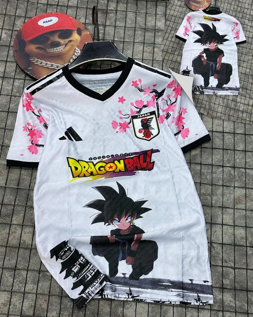 White soccer jersey featuring Dragon Ball Goku print, pink cherry blossoms, and Japan crest.