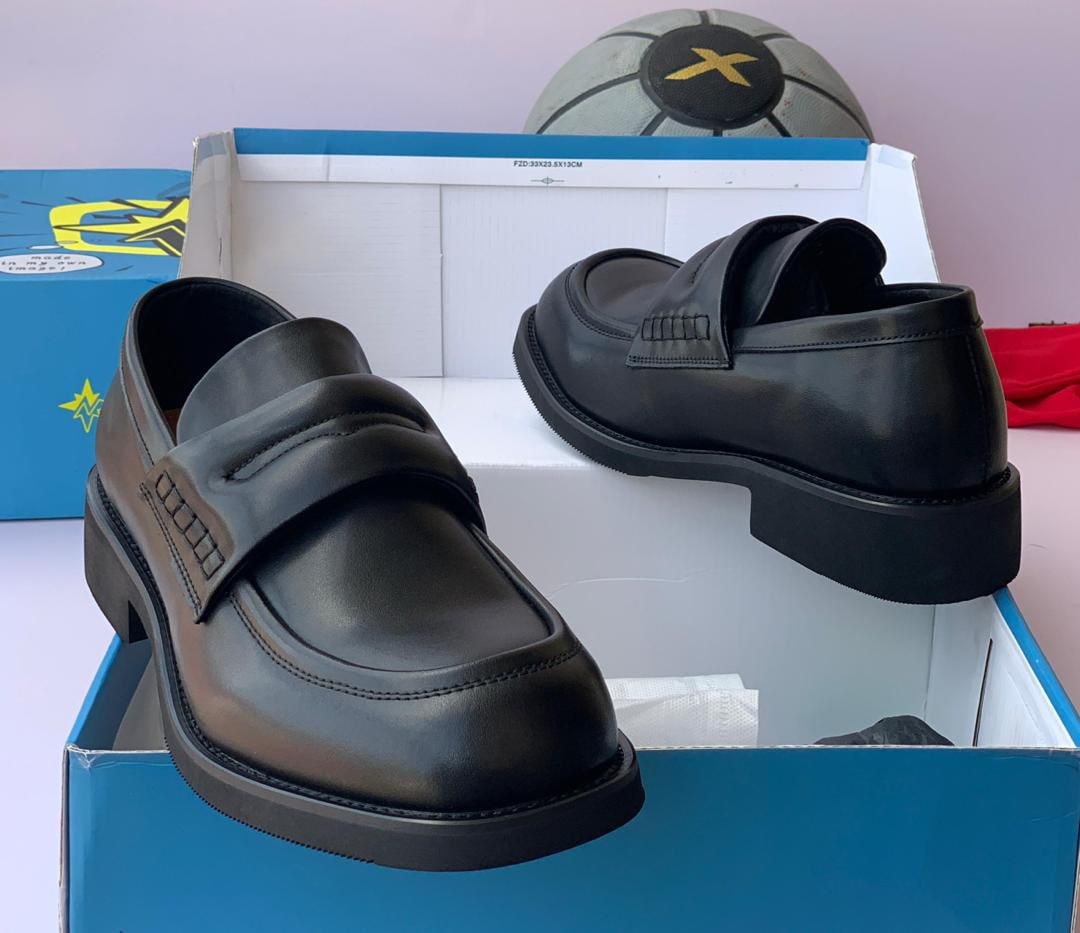 Black loafers in blue box with football prop in background.