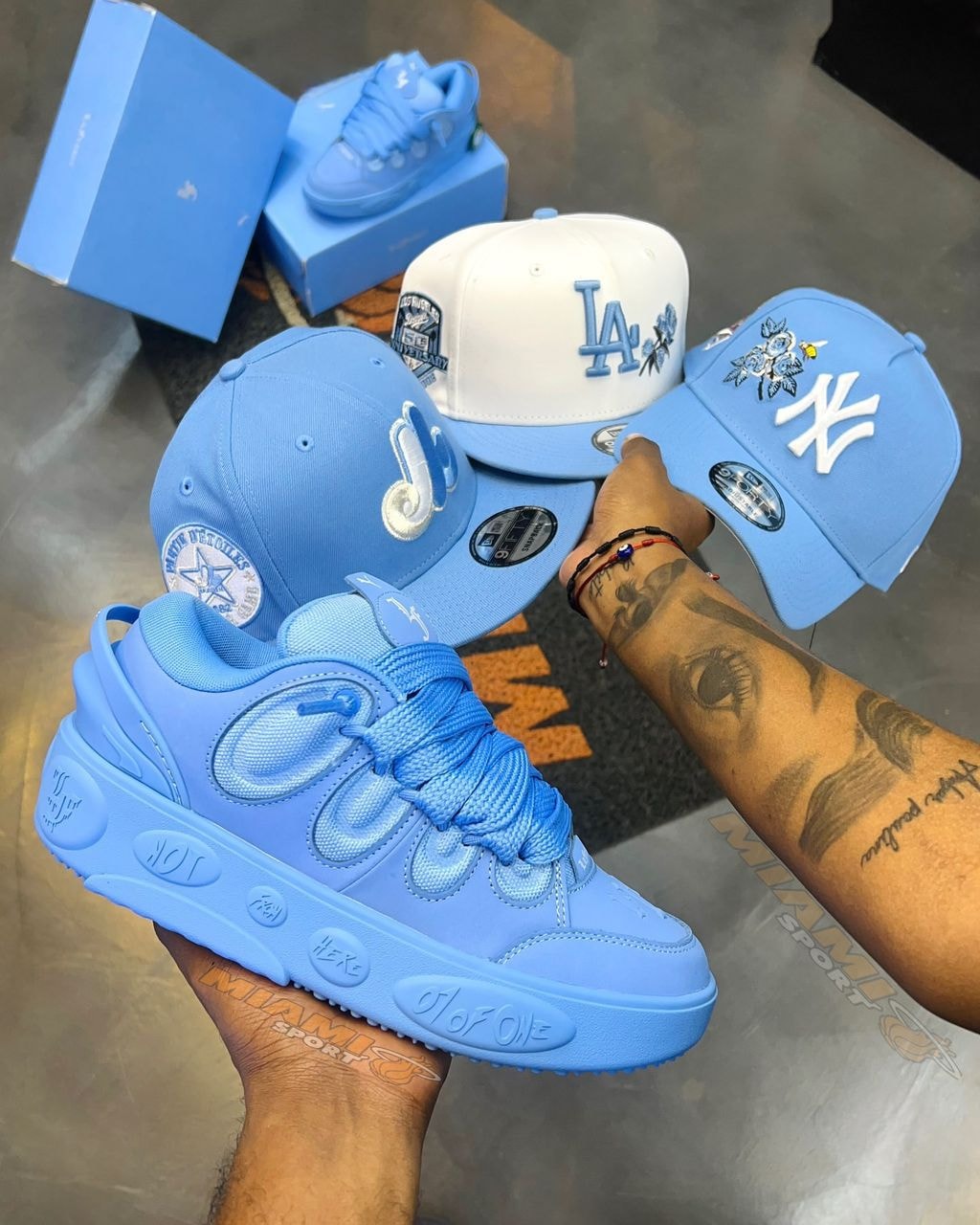 Blue chunky platform sneaker held with blue and white baseball caps in background.