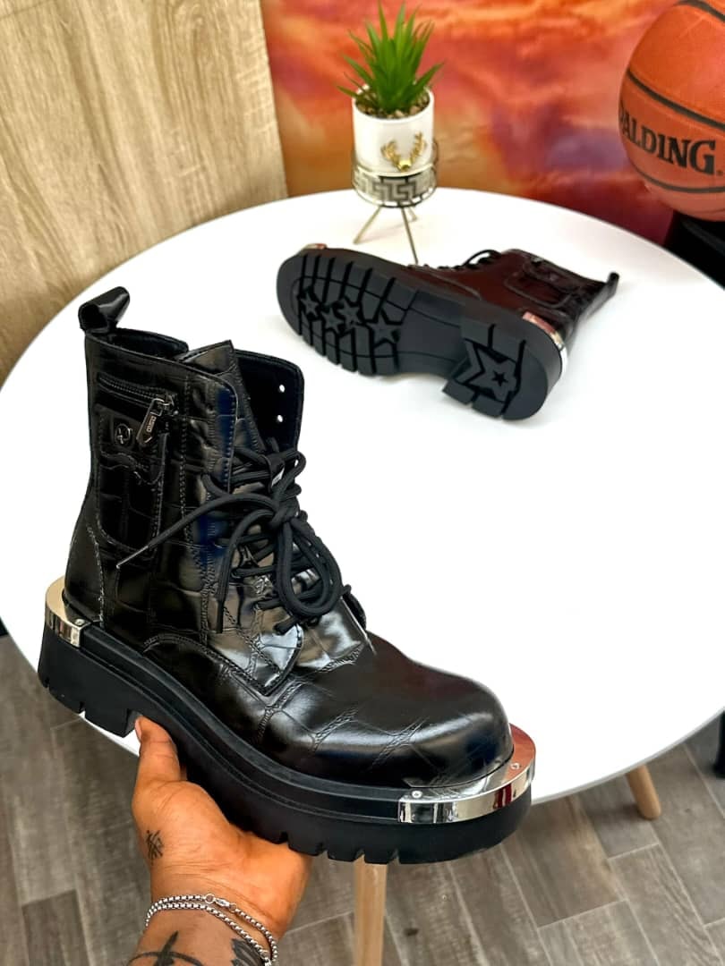 Black combat boot with laces, side zipper, metal toe cap and thick lug sole held by hand.