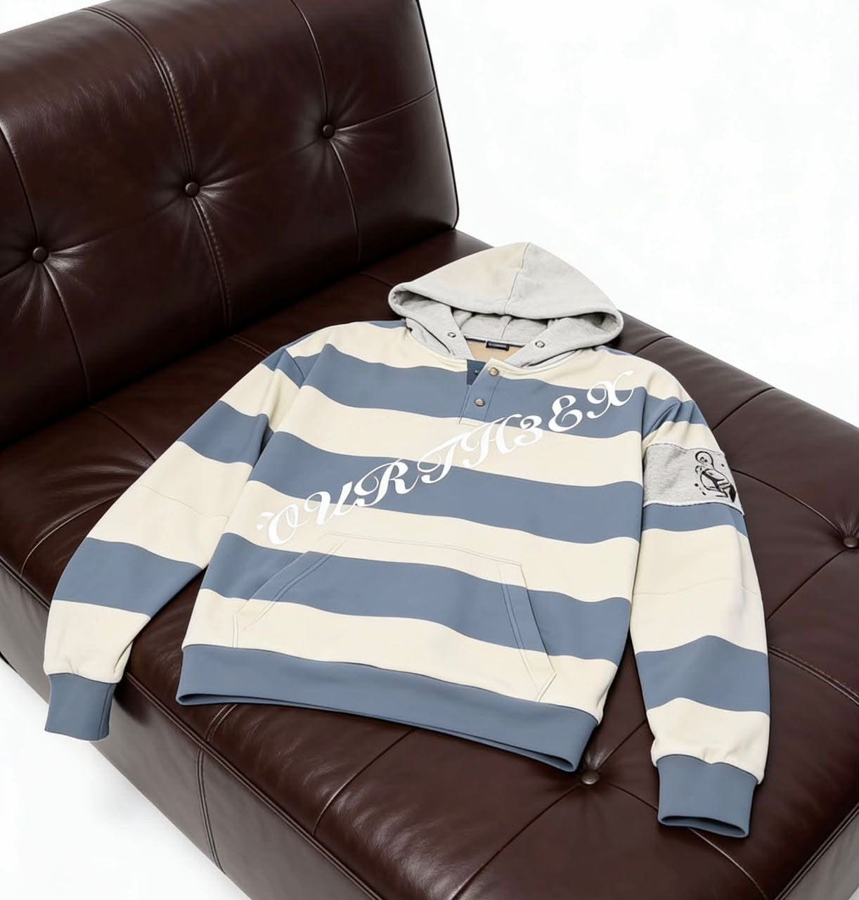 Cream and blue striped hoodie displayed on dark leather couch.