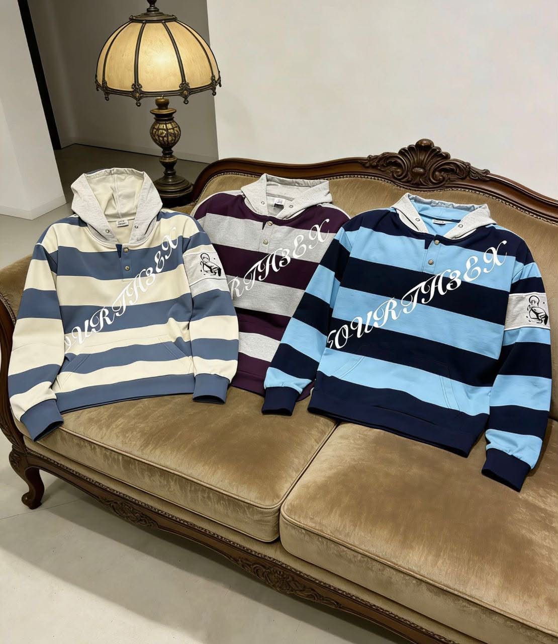 Three colorways of striped hoodie on vintage sofa: cream, purple, and blue.