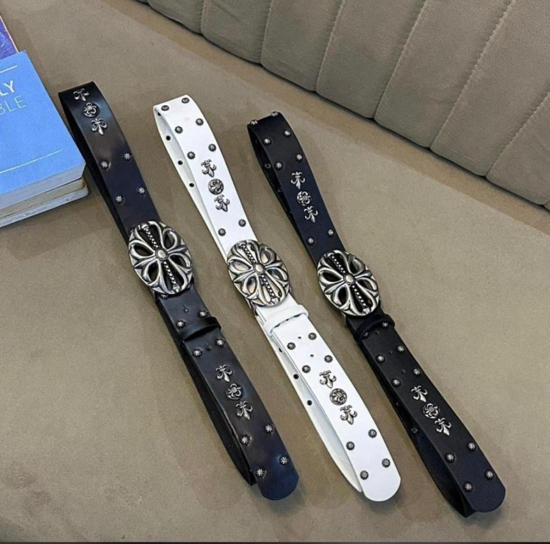 Black and white designer belts with silver ornate buckles and stud details laid flat.