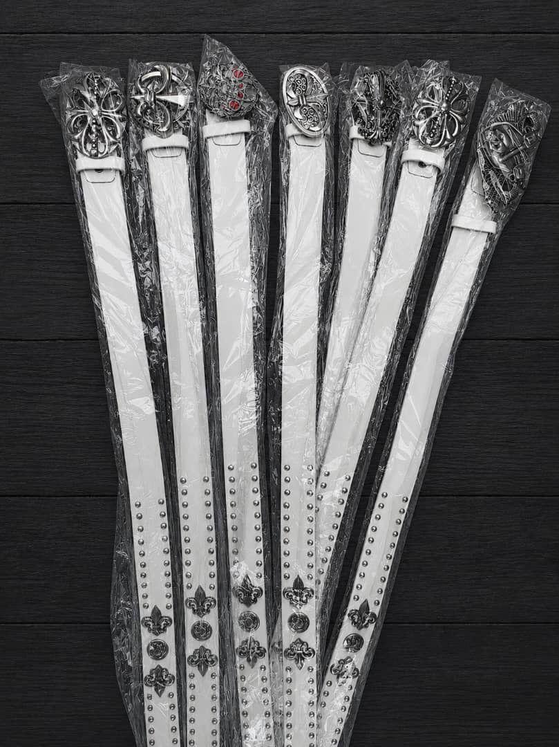 Multiple packaged white designer belts with various ornate silver buckles.