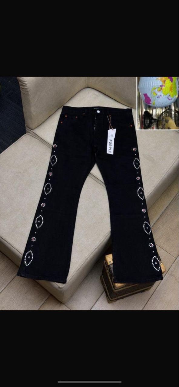 Black flared jeans with rhinestone patterns on sides shown flat on couch with tag.