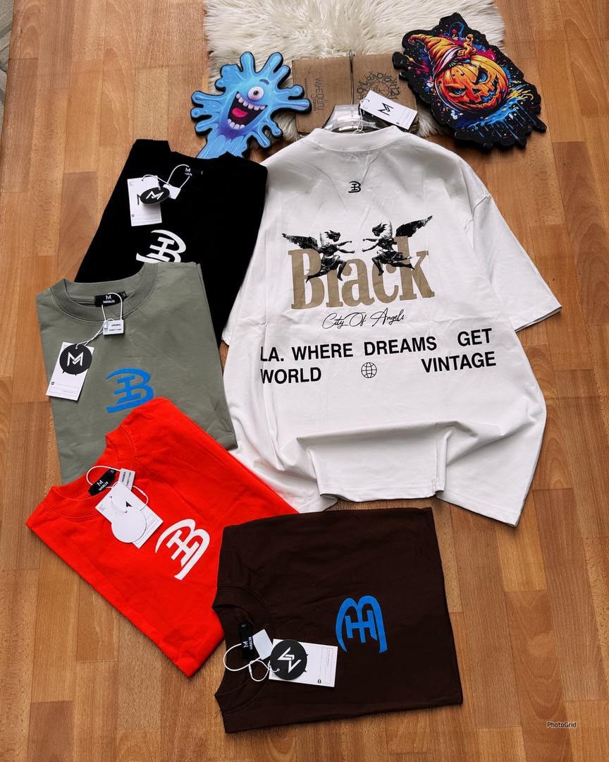 White oversized graphic t-shirt with Black City Of Angels print laid flat among folded colored tees.