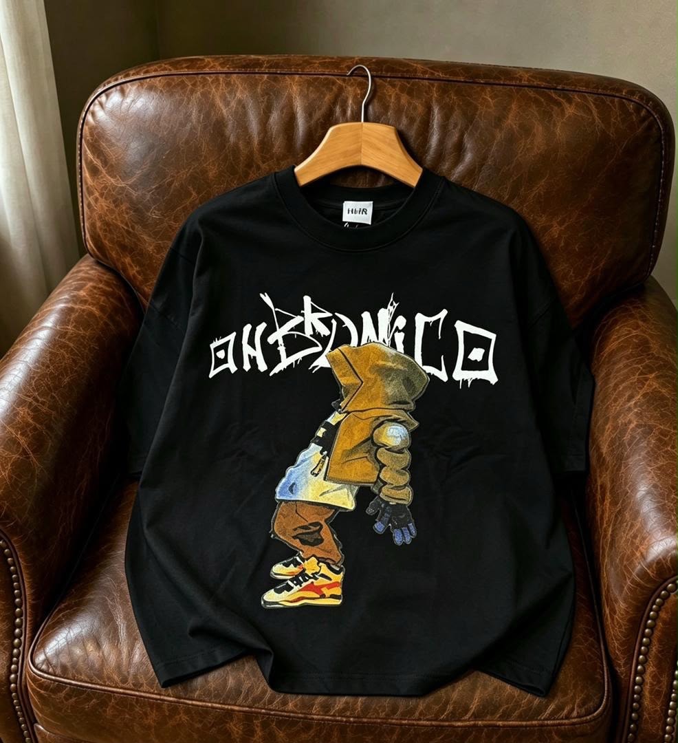 Black t-shirt with white OHKEDNICO graphic and character illustration on leather chair.