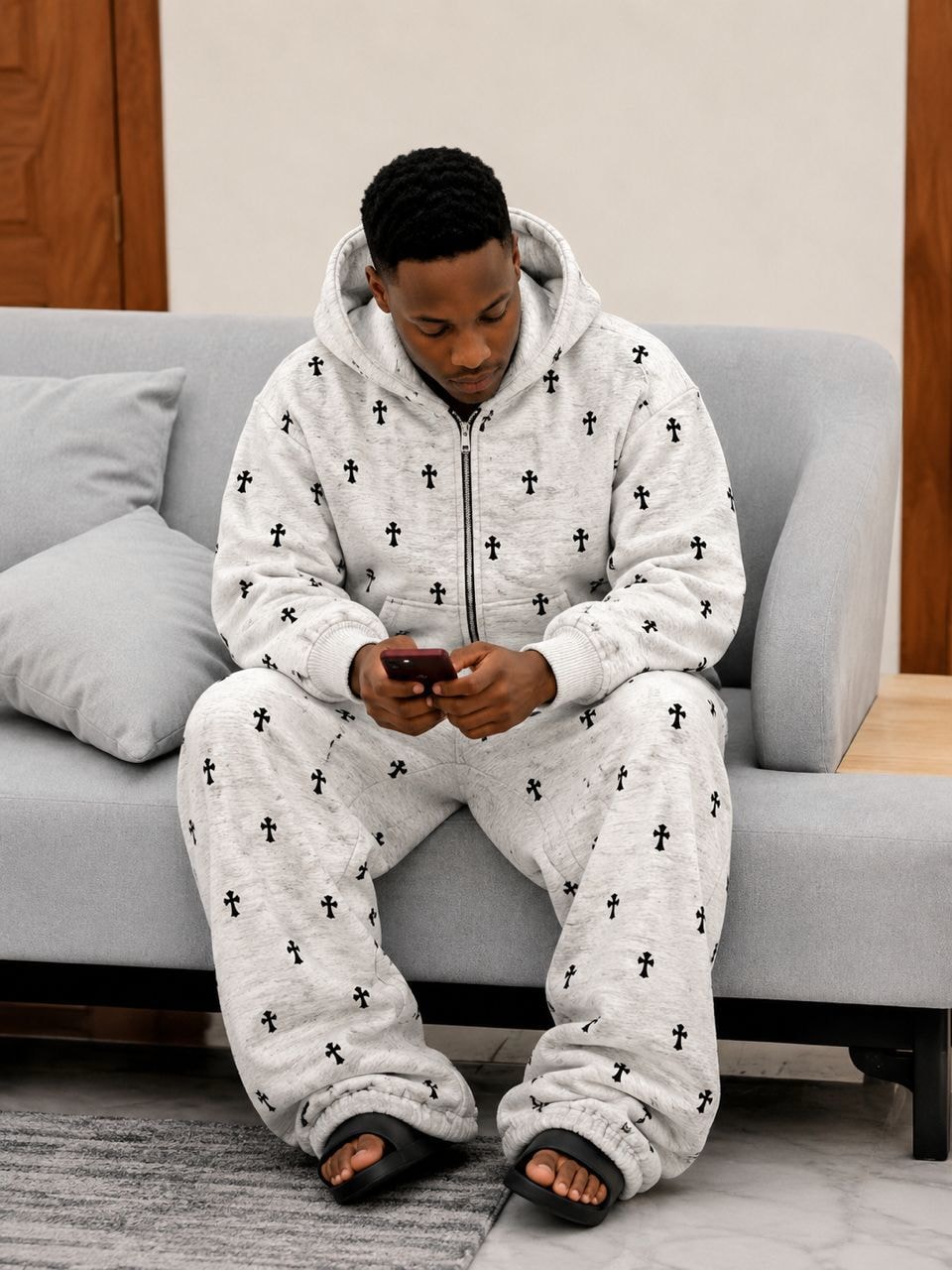Model wearing gray cross print zip-up hoodie and matching pants set while seated.