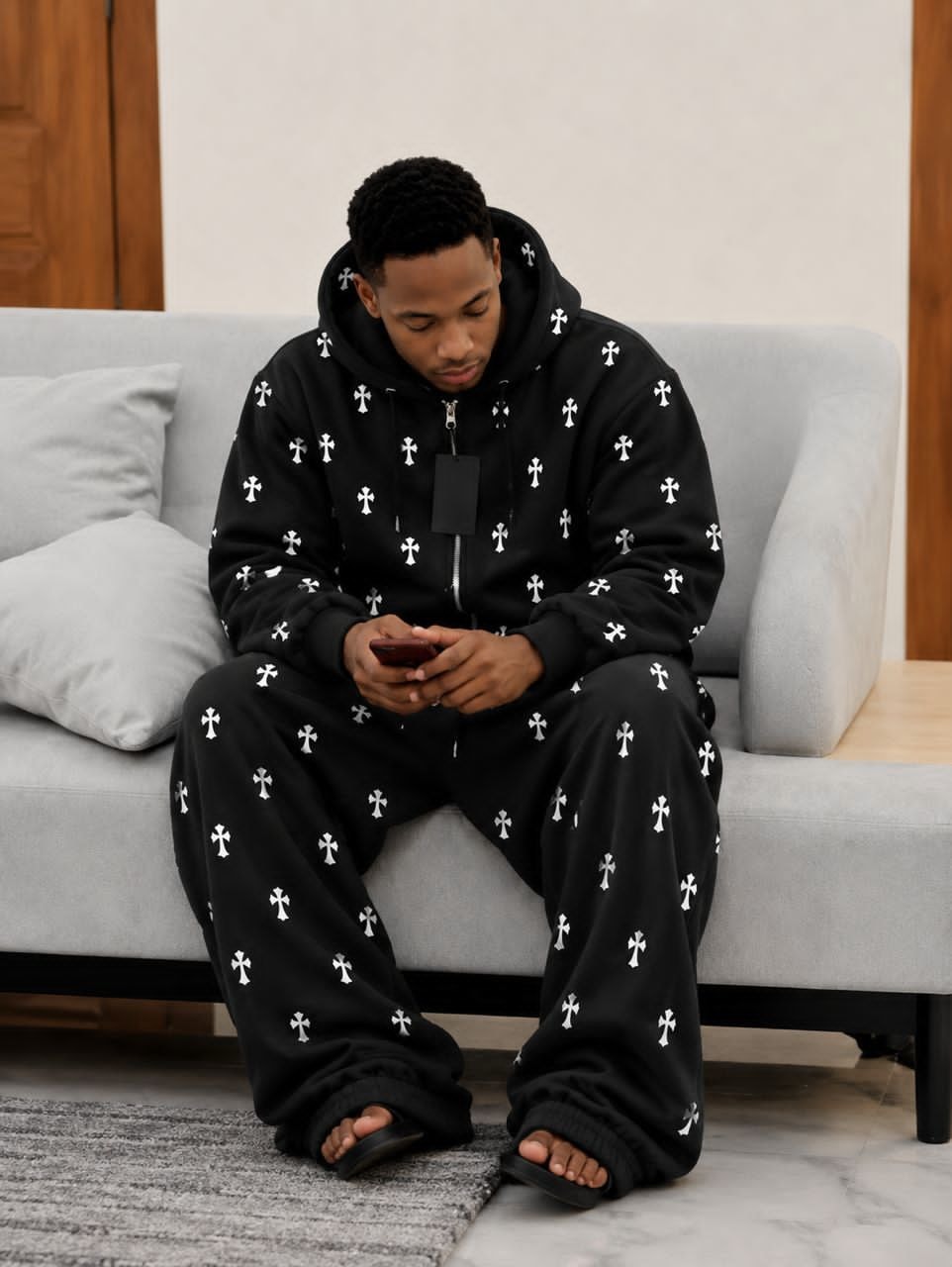 Model wearing black cross print zip-up hoodie and matching pants set while seated.