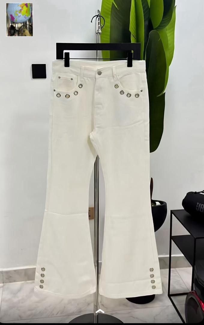 White flared jeans with silver grommets on pockets and hems displayed on hanger.